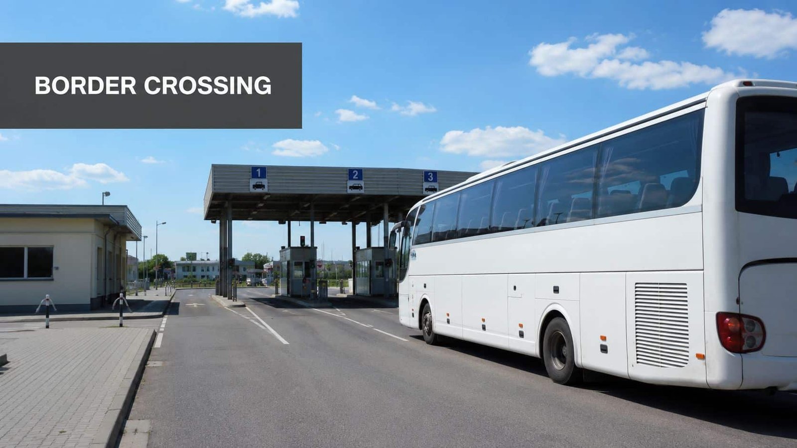 A large white bus waiting at a border crossing checkpoint with numbered lanes under a clear blue sky.