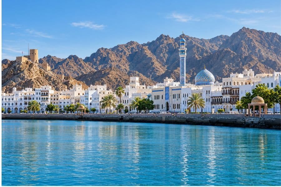 Mutrah waterfront in Muscat with a blue-domed mosque, white buildings and rugged mountains beside the harbour.