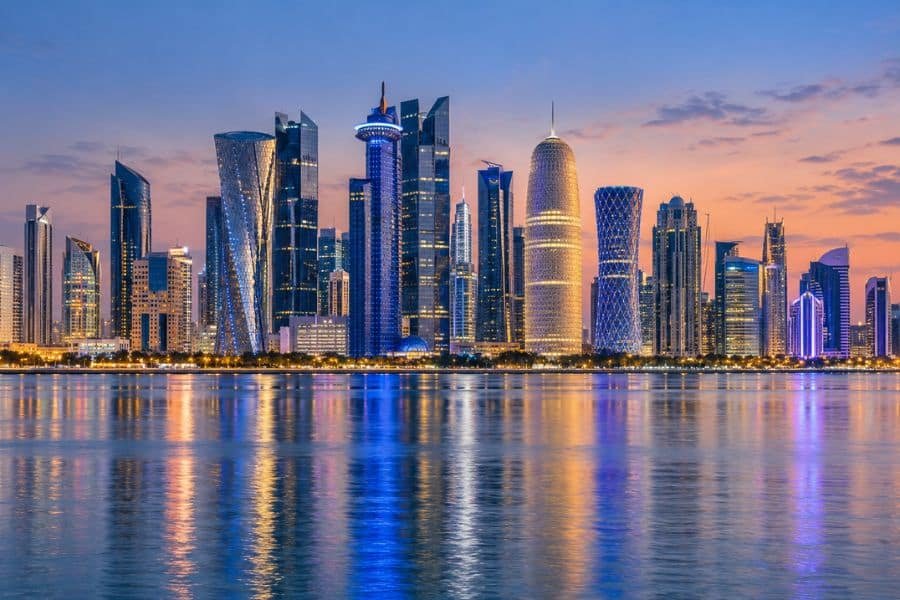 Illuminated Doha West Bay towers reflected in calm waterfront waters at dusk.